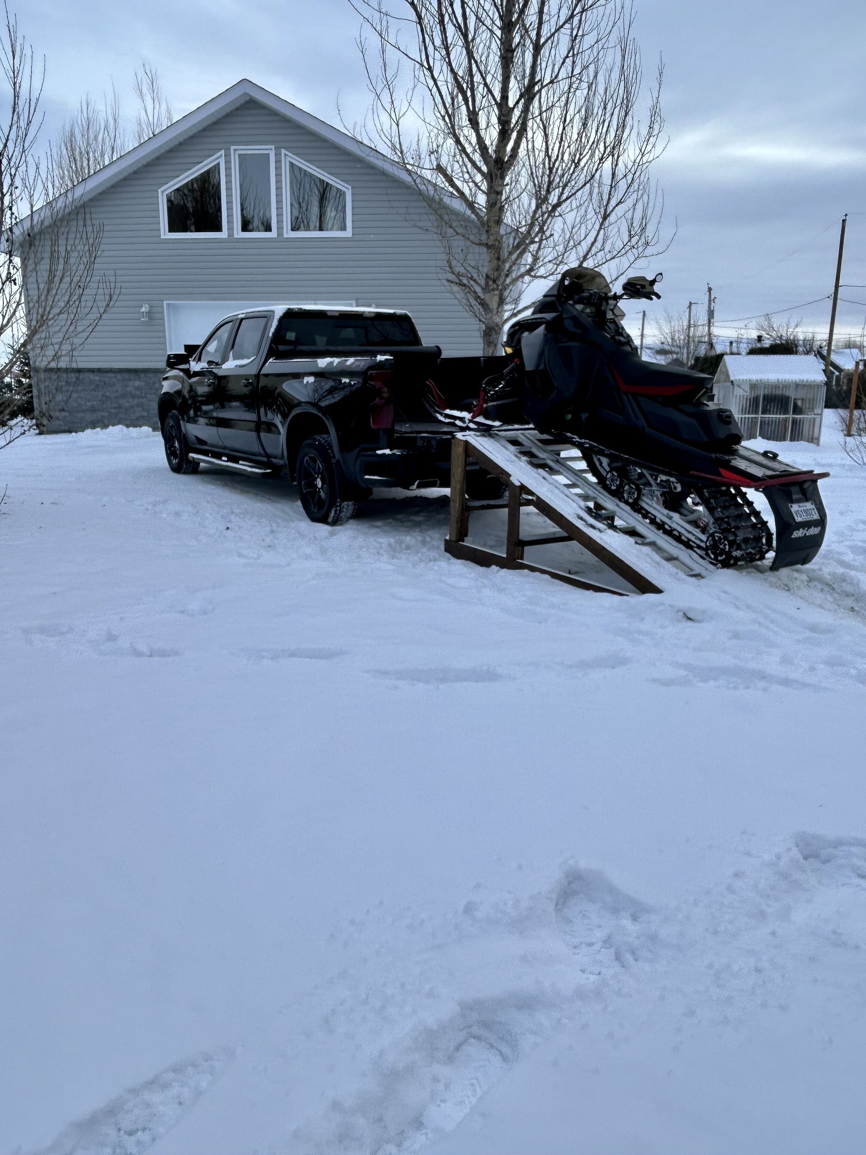 A snow-covered driveway with a pickup truck and a snowmobile.