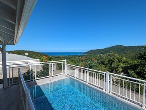 Una piscina con baranda blanca, con vistas a un paisaje costero con colinas y un cielo azul despejado.