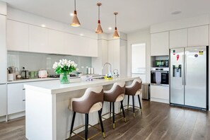 Una cucina moderna con isola centrale, sgabelli da bar, illuminazione a sospensione e un frigorifero in acciaio inossidabile.