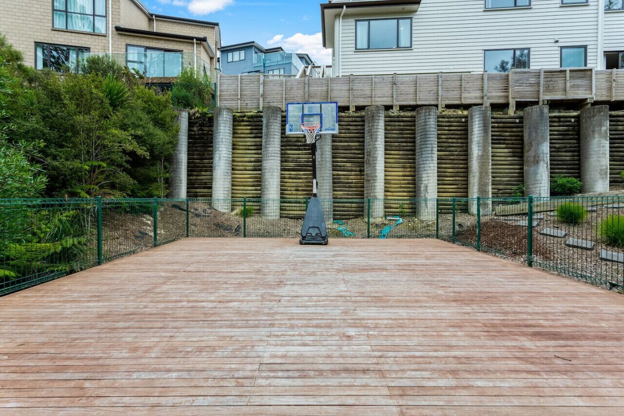 Un terrain de basket en plein air doté d’une plateforme en bois, entouré d’une clôture métallique et de verdure.