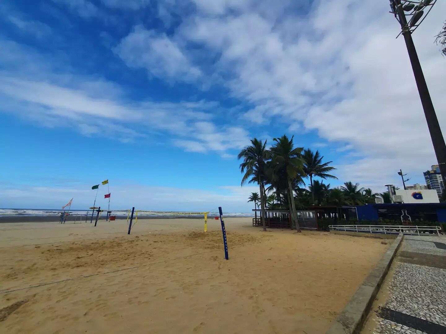 A beach with a volleyball net, palm trees, and a clear sky.