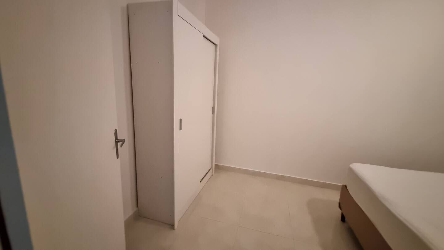 Una habitació amb una porta tancada, un llit amb matalàs blanc i un sòl de rajoles.