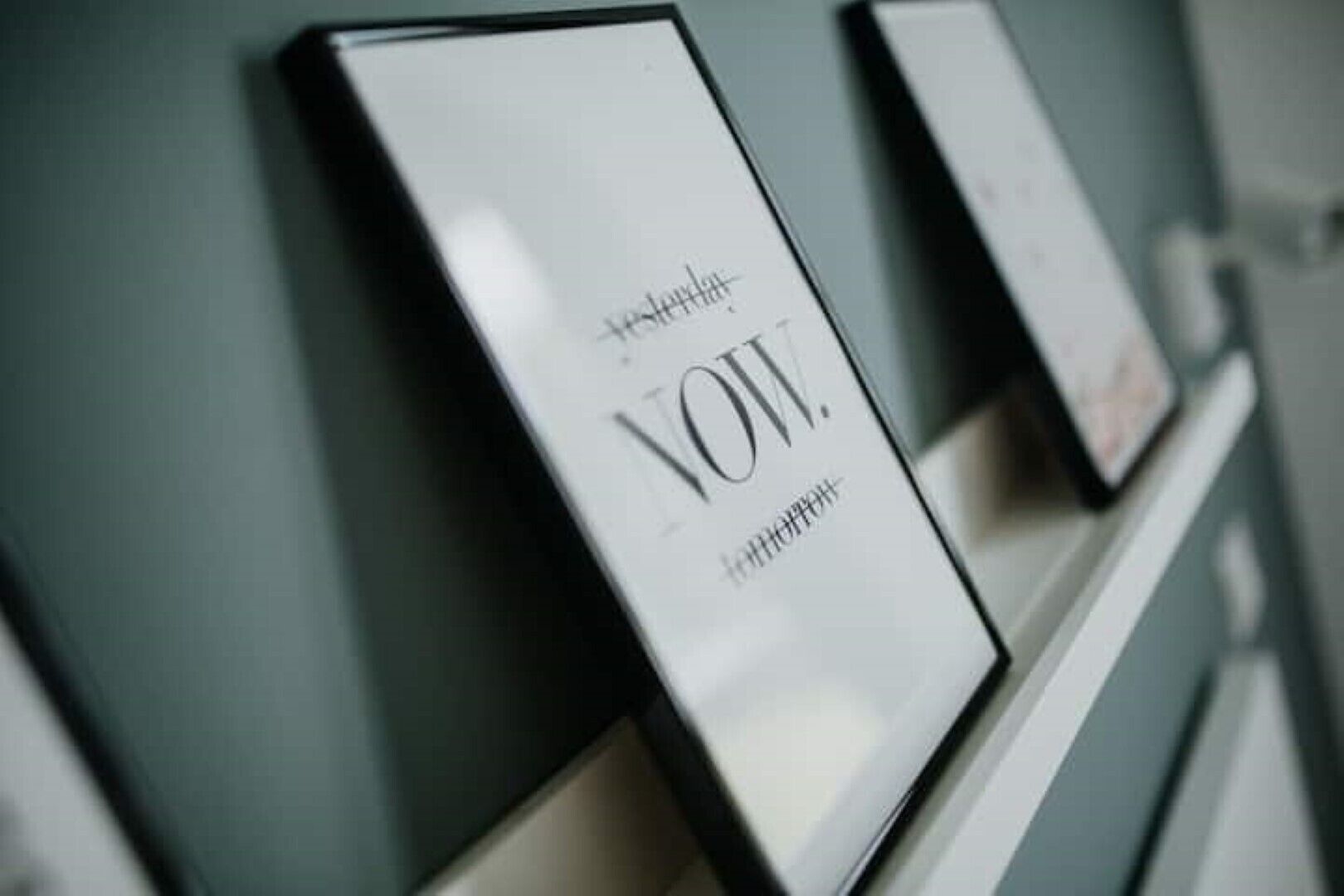Ein gerahmtes Schild mit der Aufschrift 'NOW' und 'morgen' an einer Wand.