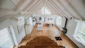 Ruime loftkamer met hoge plafonds, houten vloer en grote ramen.