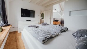 Een slaapkamer met een bed, een aan de muur bevestigde televisie, een houten bankje en een kleine keukenhoek.