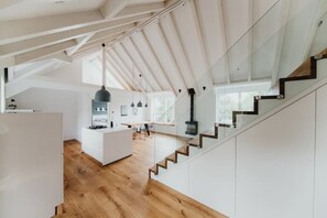 A modern kitchen with a central island, wooden flooring, and a staircase leading to an upper level. - Stadt-land-scheune - Landloft im Dachgeschoss (Braunschweig)