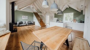 Een ruime loft met een houten eettafel, een trap en een keukenhoek.