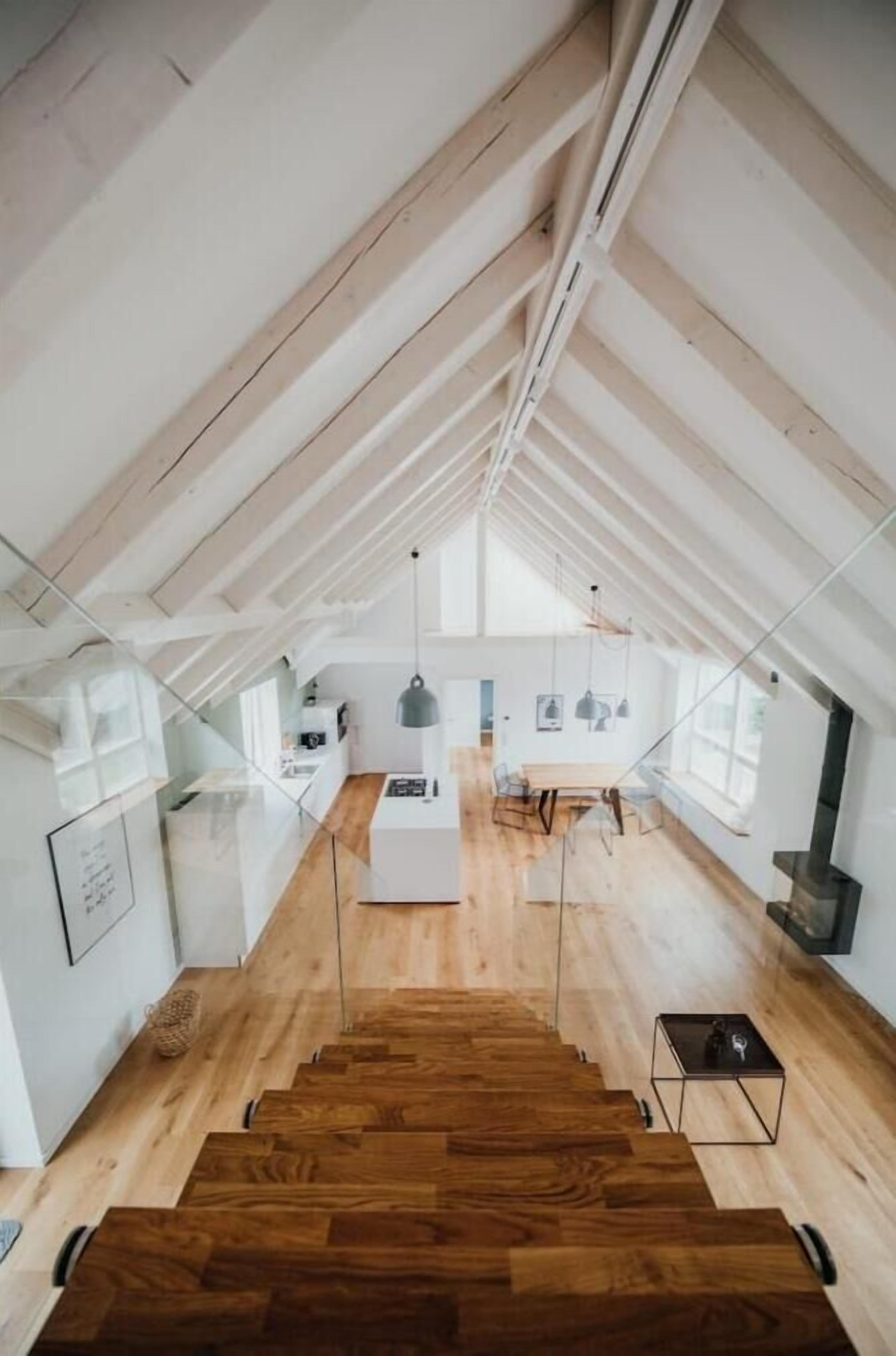 A spacious attic room with a wooden staircase leading to a kitchen area.