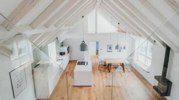 A spacious attic room with a wooden staircase leading to a kitchen area.