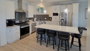 Een moderne keuken met witte kasten, een centraal eiland met barkrukken, roestvrijstalen apparatuur en een decoratief kunstwerk.