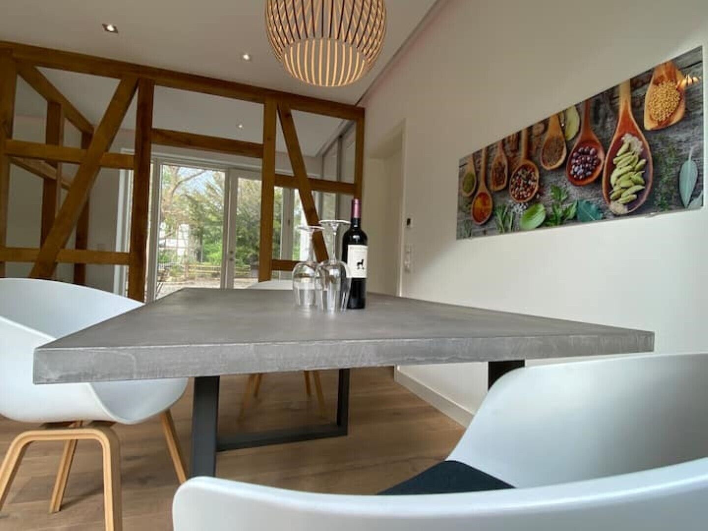 A modern dining area with a large table, white chairs, and a wine bottle.