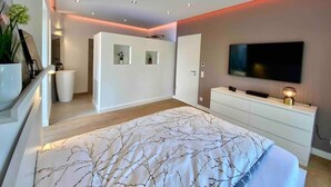 Une chambre à coucher moderne avec un grand lit, un téléviseur fixé au mur et une commode blanche.