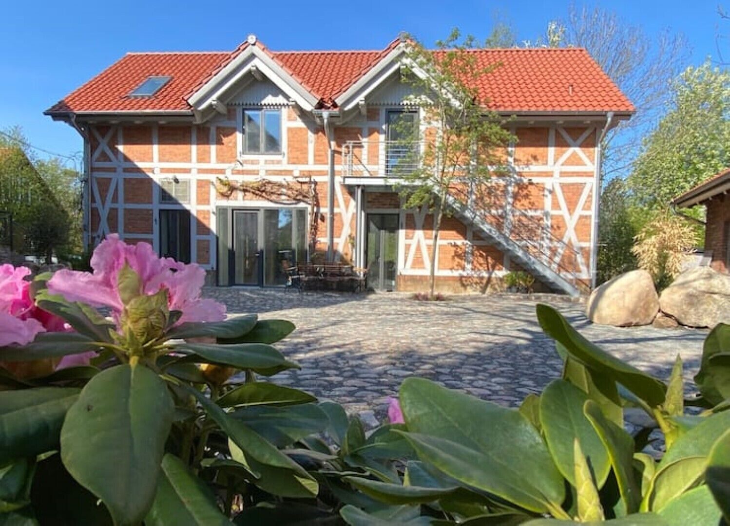 A two-story house with a red-tiled roof, a front entrance with a glass door, and a stone pathway leading to the entrance.