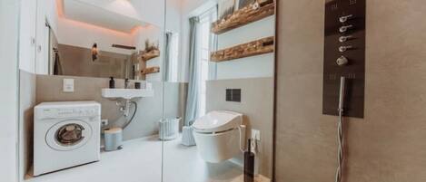 Une salle de bain moderne équipée d’un lave-linge, de toilettes et d’étagères intégrées.