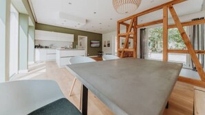 Une cuisine moderne avec des meubles blancs, un coin repas doté d’une grande table et une structure de plafond en bois.