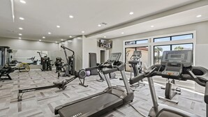 Un gimnasio moderno con diversos equipos de ejercicio, ventanas amplias y un televisor en la pared.