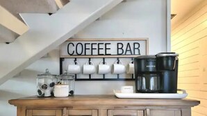 Un espacio de cafetería con un letrero, tazas, una cafetera y recipientes de almacenamiento.