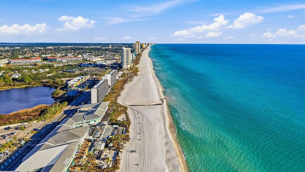 Vista aérea de una ciudad costera con una playa extensa, aguas azules cristalinas y una combinación de edificios residenciales y comerciales.