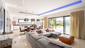 A modern living room with a sectional sofa, a dining area, and a kitchen.