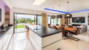 A modern kitchen with a central island, dining area with a wooden table and chairs, and a living area with a sofa and TV.