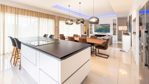 A modern kitchen with a central island, dining area with chairs, and a TV in the background.