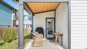 A covered patio with a wicker chair and a small table, a sliding glass door, and a wooden ceiling.