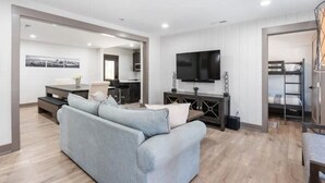 A modern living room with a grey sofa, a flat-screen TV, and a dining area with a table and chairs.