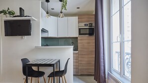 A compact kitchen with a dining area, a TV mounted on the wall, and a window with curtains.