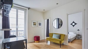 A modern, well-lit room with a dining area, a sofa, a bed, and a mirror.
