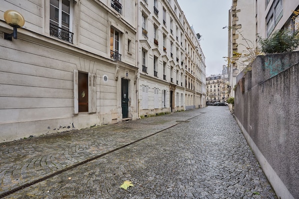 A narrow cobblestone street flanked by historic buildings with classic architecture, large windows, and decorative iron railings. - Alma - Studio Apartment, Sleeps 2 (Paris)