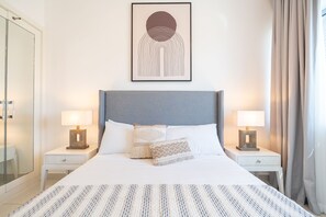 Uma cama bem arrumada com colcha listrada, duas mesas de cabeceira com abajures e uma obra de arte emoldurada acima da cama.