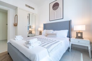 A modern bedroom with a large bed, two bedside tables with lamps, a wardrobe, and a framed artwork on the wall. - Luxury Three Bedroom in Damac Maison Near Dubai Mall by Sojo Stay (Dubai)