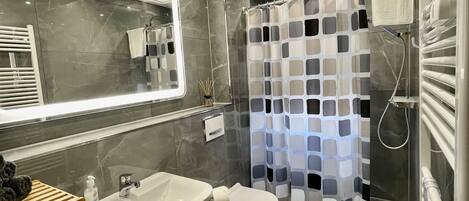 A modern bathroom with a large mirror, a sink, a toilet, and a shower with a patterned curtain.