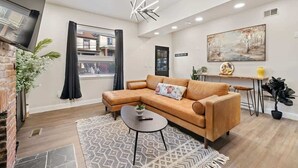 A modern living room with a leather sofa, a small coffee table, and a large window. - Colorful Home with Deck • Near Acrisure Stadium & Downtown (Pittsburgh)