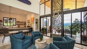 Un vaste espace de vie avec une grande fenêtre, une cuisine à l’arrière-plan et un coin repas avec des chaises et une table.