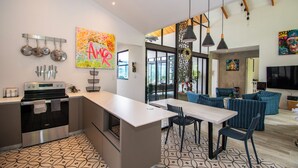 Une cuisine moderne dotée d’un îlot central, un coin repas avec une table et des chaises, et un espace de vie avec un canapé et un téléviseur.