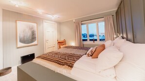 A bedroom with a large bed, a window with curtains, a door, and a framed picture on the wall. - In the middle of Lofoten! Unique and spacious dockside apartment. (STAMSUND)