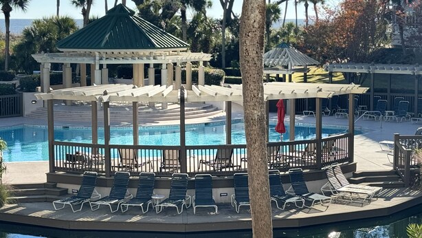 Un área de piscina con sillas de descanso, un pabellón y vista al océano.