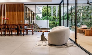 Un intérieur moderne comprenant un coin repas, un fauteuil confortable et une vue sur la verdure grâce à de grandes fenêtres en verre.