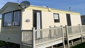 A mobile home with a deck, satellite dish, and a logo on the side. - Beach Vibes - Silver Beach - Basic (Skegness)
