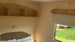 A bedroom with a bed, a headboard, a window with a view of a green field, and a ceiling light. - Beach Vibes - Silver Beach - Basic (Skegness)