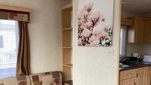 Un espacio habitable compacto con sofá, área de cocina y un cuadro con flores rosas colgado en la pared.