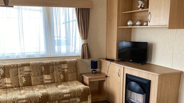 A cozy living area with a sofa, a television, a small table, and a fireplace. - Beach Daze - Silver Beach - Standard (Skegness)