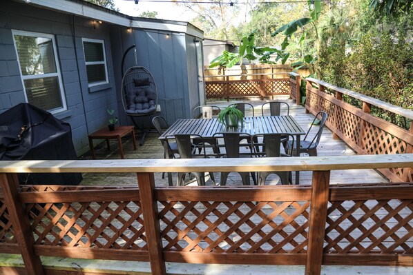 Une terrasse avec une table et des chaises en bois, un fauteuil suspendu et un barbecue.