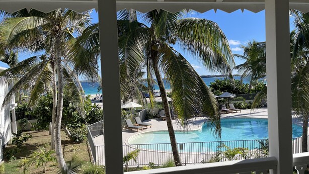A poolside view with palm trees, a clear blue sky, and a view of the ocean. - Bella Vista 2 bedroom - Orient Bay (Collectivité de Saint-Martin)