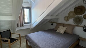 A bedroom with a sloped ceiling, a bed, a chair, and a window. - Bella Vista 2 bedroom - Orient Bay (Collectivité de Saint-Martin)