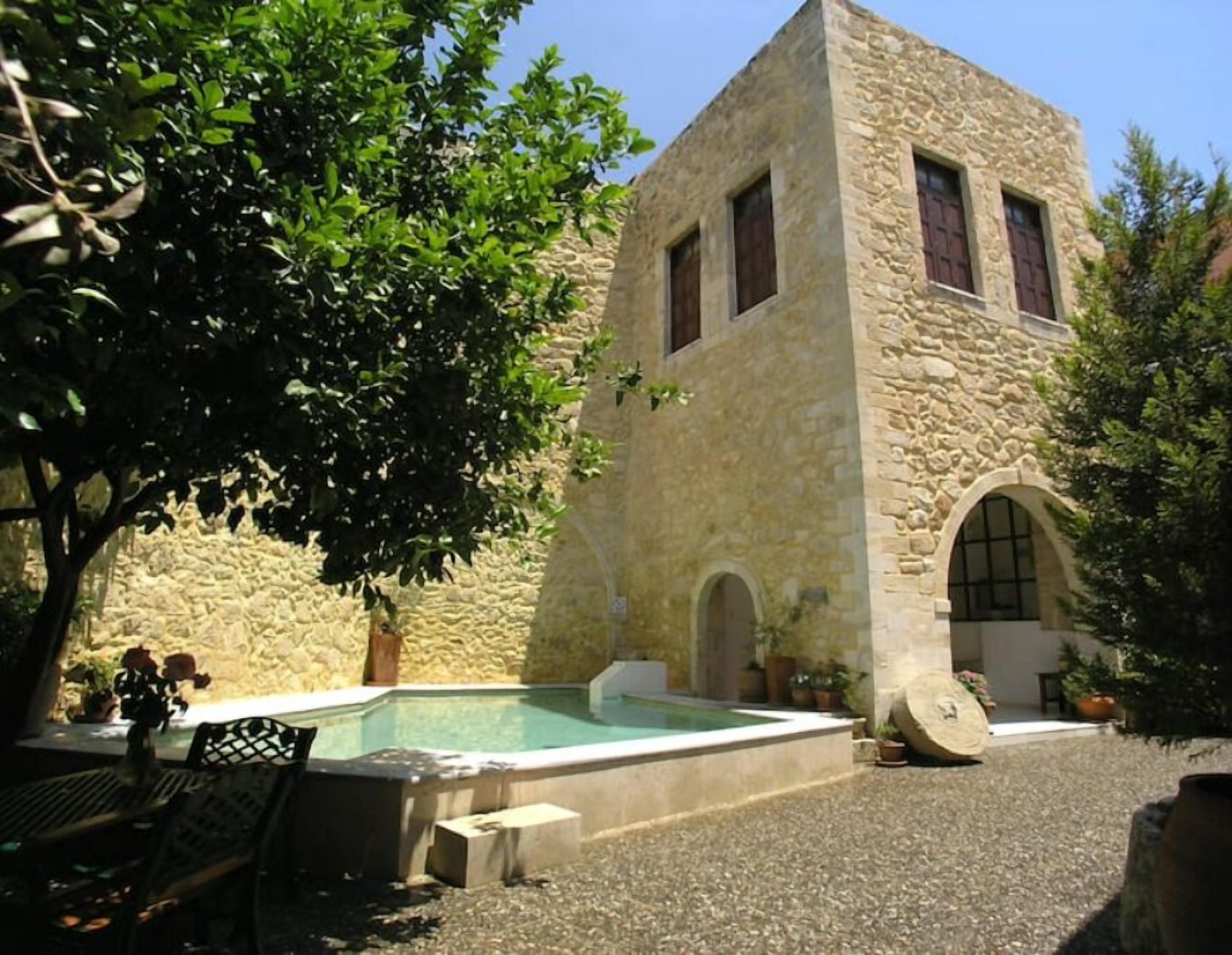A stone building with a pool, benches, and potted plants.