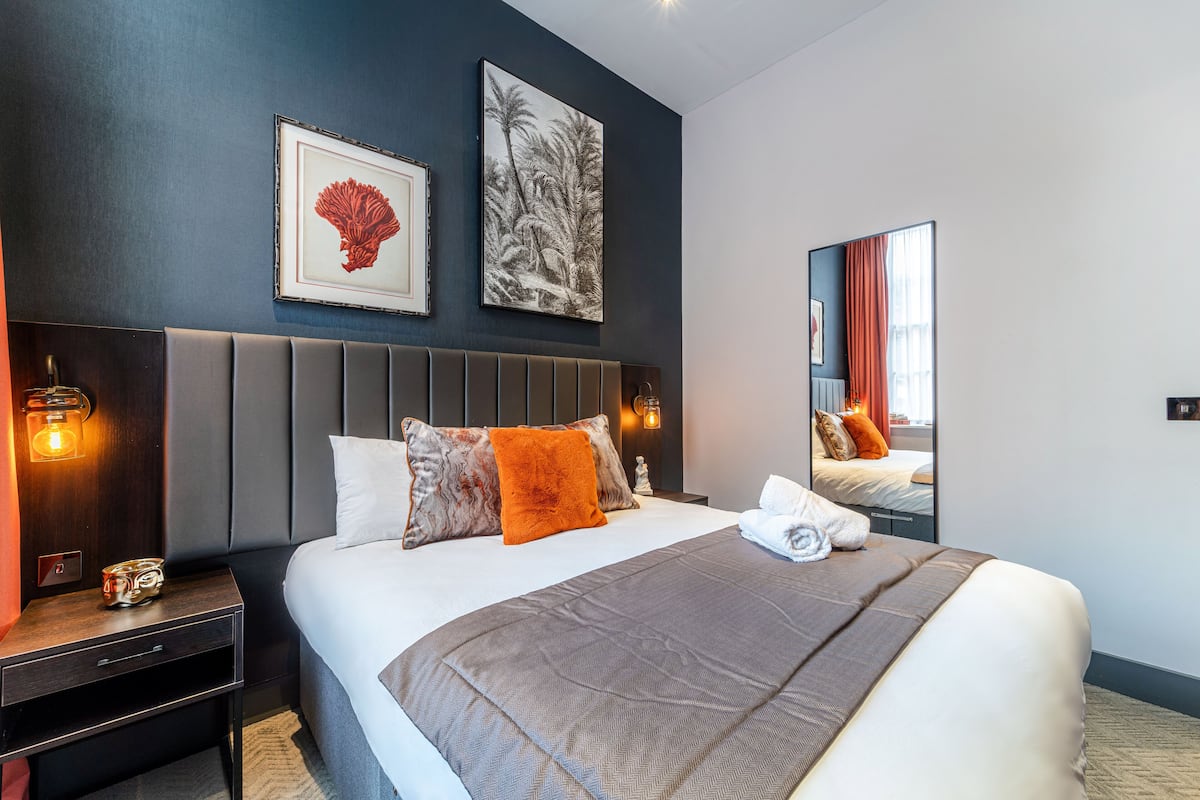 A modern hotel room with a large bed, a headboard, a nightstand, and a mirror.