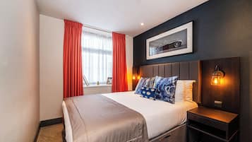 A hotel room with a large bed, a nightstand, a wall-mounted light, and a framed picture above the bed.