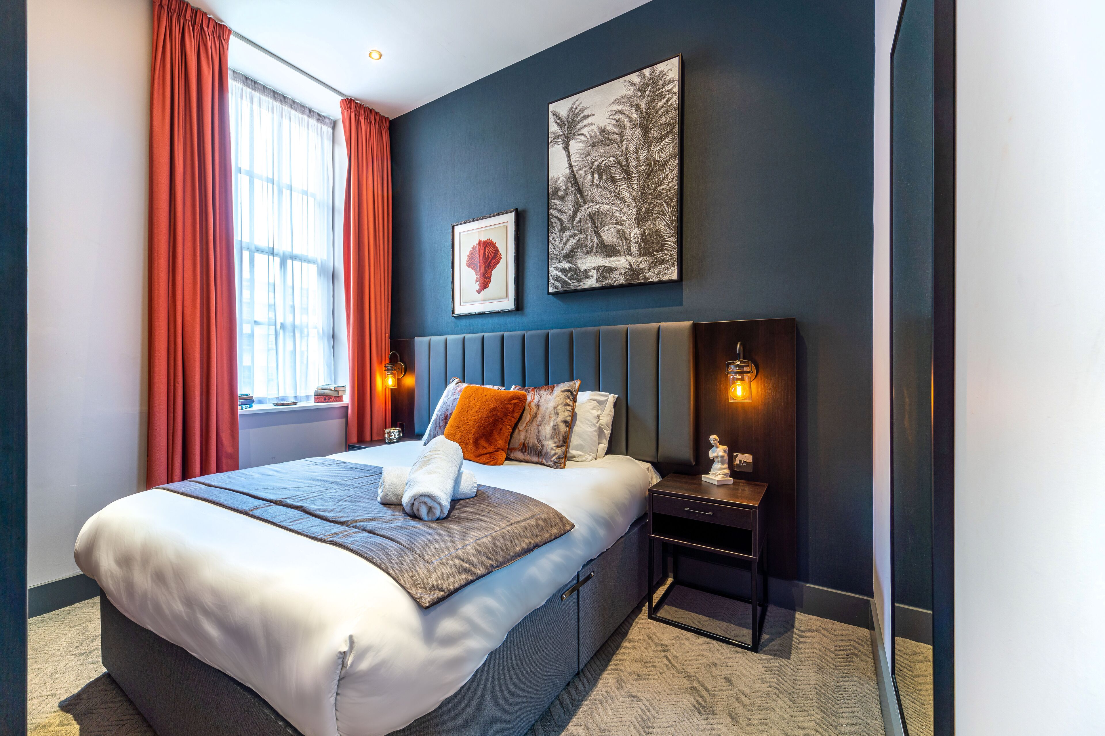 Une chambre d’hôtel moderne avec un grand lit, une table de chevet, une lampe fixée au mur et une fenêtre avec des rideaux.